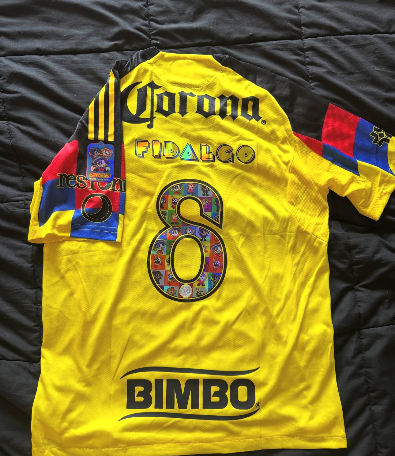 A yellow soccer jersey with various logos and text on it, laid out on a black surface.